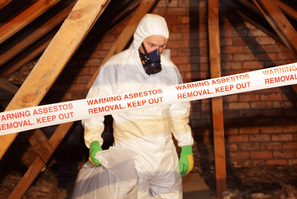 A worker wearing protective clothing while clearing asbestos from an old attic.