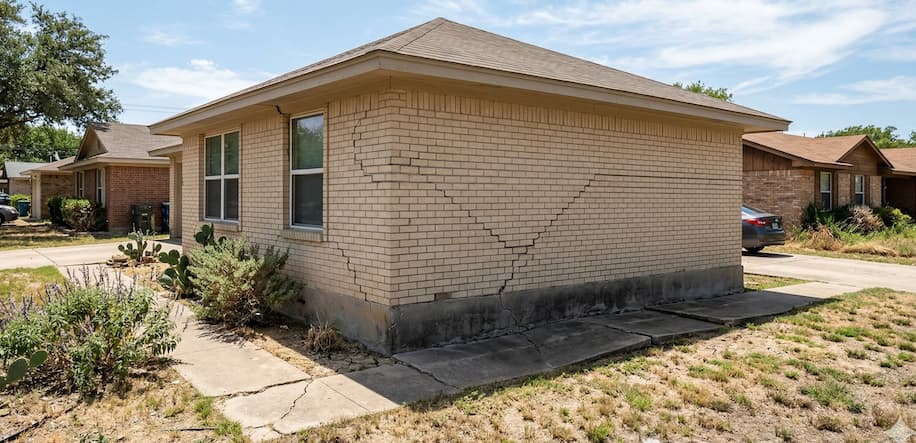 Brick house with noticeable wall crack and dry lawn.