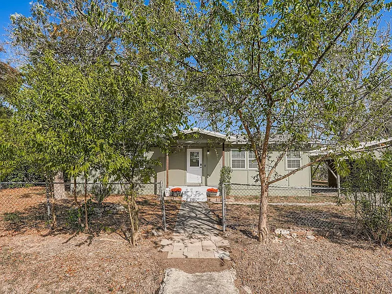 Green house partially hidden by trees with a path leading to the front door.